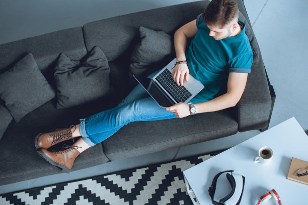 年轻人坐在家里的沙发上用笔记本电脑工作的俯视图图片下载