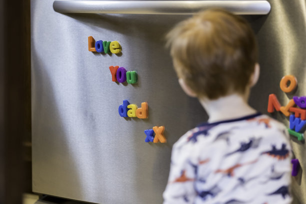 可爱的小男孩在玩冰箱上的磁铁文字，我爱爸爸图片下载
