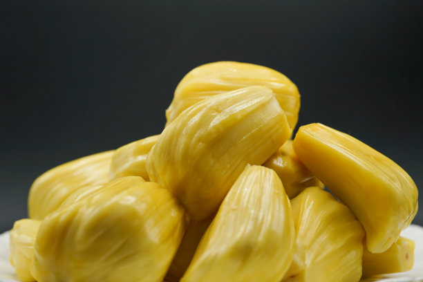 新鲜的菠萝蜜切片放在白色的盘子里。香甜的黄色菠萝蜜成熟了。素食者，纯素食者，生食。奇异的热带水果-特写孤立素材图片