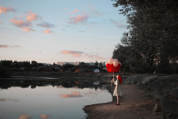 红发女孩拿着红白相间的气球在大自然中映衬着天空。快乐的女人。艺术照片图片下载