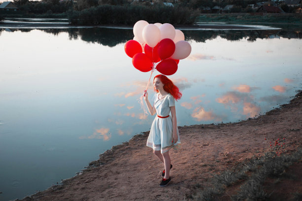 红发女孩拿着红白相间的气球在大自然中映衬着天空。快乐的女人。艺术照片图片下载