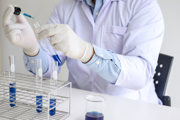 科学家或医务人员穿着白大褂，手持试管，试管中有彩色液体滴在玻璃上，从事生物化学实验室研究图片下载