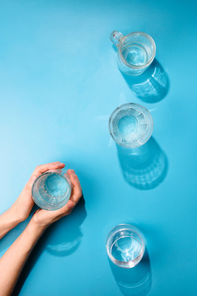 扁平的女人的手拿着一杯干净的苏打水。健康理念，蓝色背景图片下载