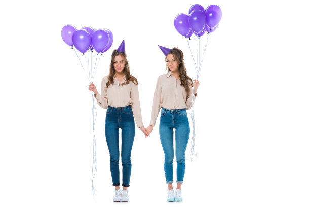 迷人的年轻双胞胎与紫罗兰气球手孤立的白色图片下载