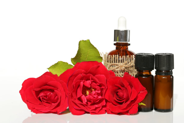 天然玫瑰精油。玫瑰油在棕色的玻璃瓶和大的红色玫瑰在白色的背景。有机天然油图片下载