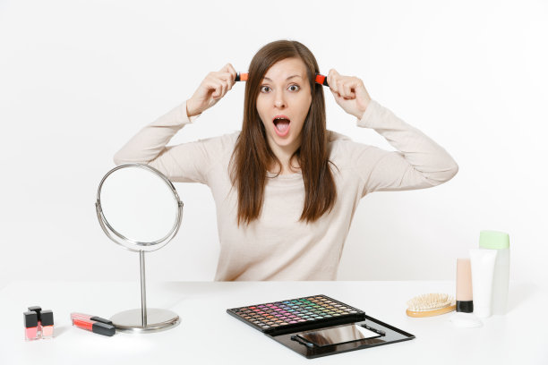 有趣的年轻女子坐在餐桌与指甲油，应用化妆与设置面部装饰化妆品隔离在白色的背景。美丽女性时尚生活理念。有拷贝空间的区域。图片下载