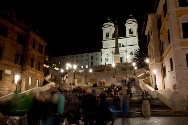 一个广场的水平视图广场在晚上与模糊的人和教堂的台阶称为Trinità dei Monti照明的人造灯光在夜空背景。图片下载