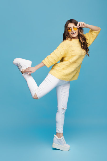 迷人的年轻女士在蓝色的背景摆姿势。漂亮女孩跳舞，玩得很开心。头发飞。图片下载