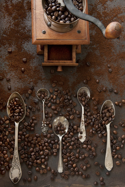 近距离照片的金属汤匙与香气的咖啡豆和咖啡豆研磨机在黑色的桌子背景图片下载
