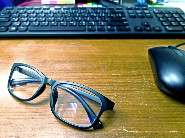 旧的木桌上放着眼镜，电脑键盘和鼠标背景模糊不清图片下载