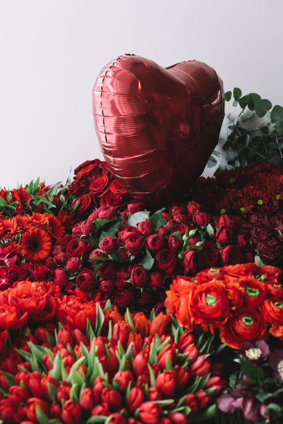 红色心形气球上排列着一朵朵鲜艳的鲜花，以鲜艳的红色为背景，花店新鲜送花图片下载