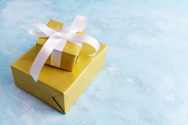 两个礼品盒在金色的纸与白色蝴蝶结在蓝色的背景。节日的概念。新年，圣诞节，生日礼物。文本空间素材图片