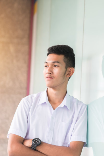 英俊的亚洲青年学生站在外面看风景，穿着白衬衫制服图片下载