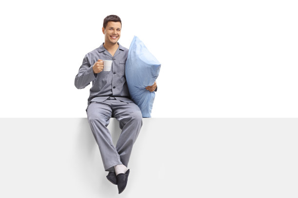 一个穿着睡衣的年轻人，手里拿着一个杯子和一个枕头，坐在一个嵌板上图片下载