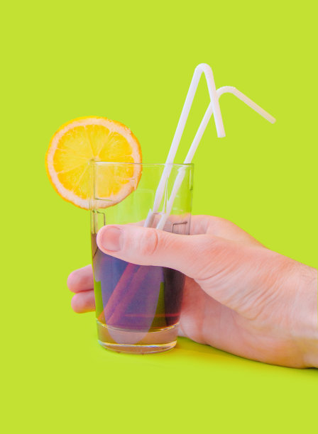 手握新鲜果汁杯与黄色柠檬草片在一个绿色的背景图片下载