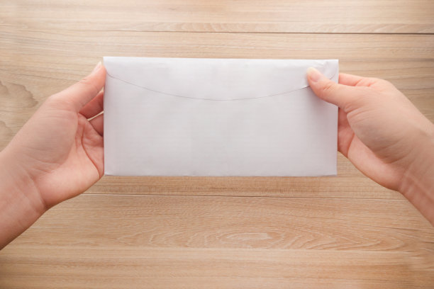女人的手拿着一个白色的长纸信封或信封放在木桌上，俯视图背景。图片下载