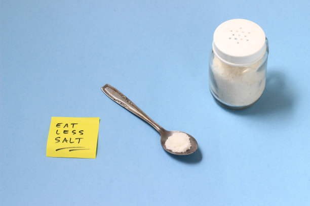 健康生活方式插画：茶匙中的盐，摇壶，带有“少吃盐”字样的黄色便签，蓝色背景图片下载