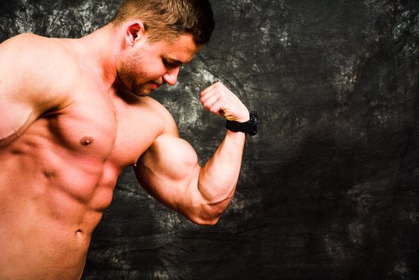 健美运动员在黑暗的背景下收缩肌肉图片下载