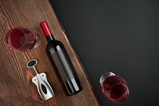 在黑色背景的木板上有一个开瓶器、一瓶葡萄酒和两个玻璃杯。顶部视图与复制空间素材图片