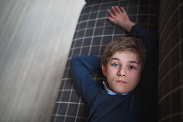 一个穿着蓝色衬衫、长着蓝色眼睛的少年躺在一个白色笼子里的蓝色沙发上，近距离地看着镜头。图片下载