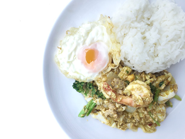 用黄咖喱粉和泰式草本蔬菜炒对虾、鱿鱼和海鲜，配以米饭和炒蛋，白底。泰国风格的食物。图片下载