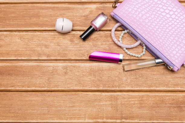 木质背景的女人钱包里的东西。女士的化妆品从粉色手提包里掉了出来。前视图。图片下载