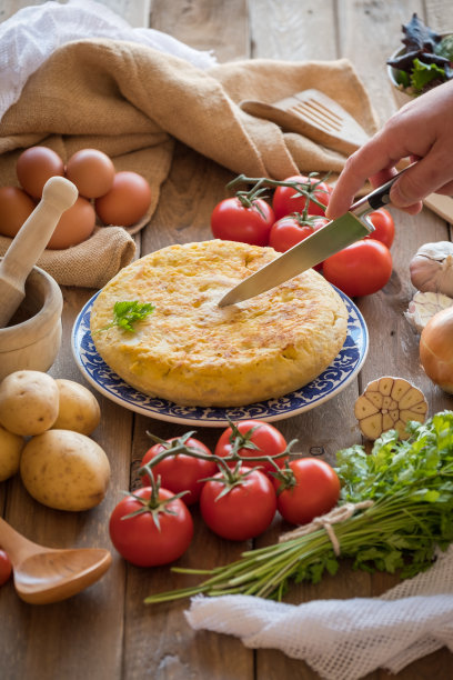 厨师正在切一个传统的西班牙煎蛋卷近距离，从上面看。西班牙玉米粉圆饼，质朴的木质质地图片下载