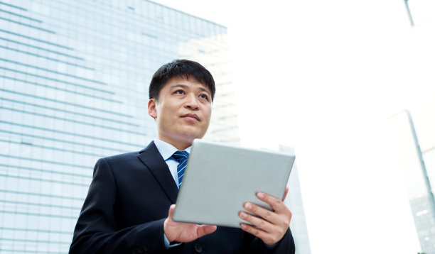 商人在办公大楼前使用平板电脑素材图片