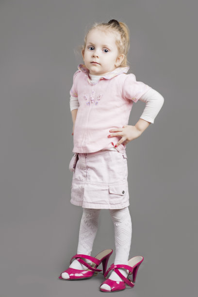 严肃的白人女孩的肖像穿着母亲的父母高跟鞋。图片下载