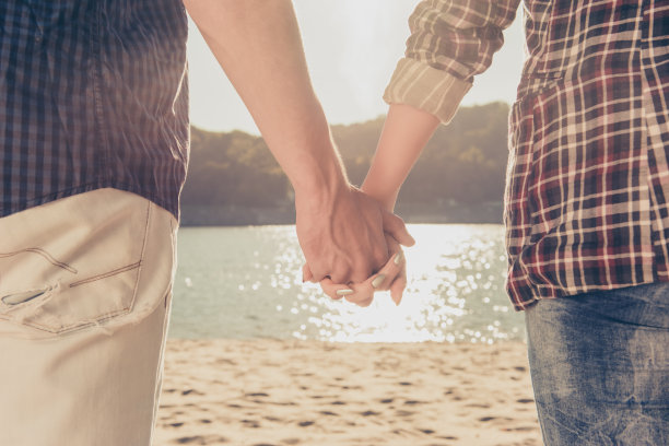 男人和女人在海边牵着手在日落的近距离照片图片下载