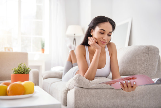 可爱的年轻女子躺在沙发上看杂志图片下载