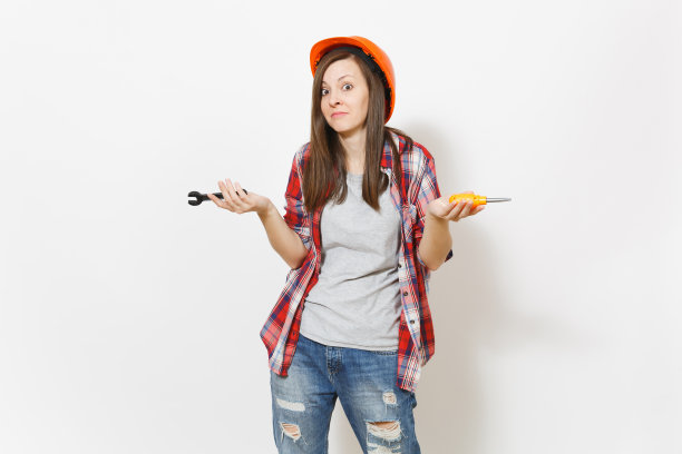 年轻不满的女人在保护施工橙色头盔拿着玩具螺丝刀和扳手隔离在白色的背景。用于装修公寓房间的仪器。修理家里的概念。图片下载