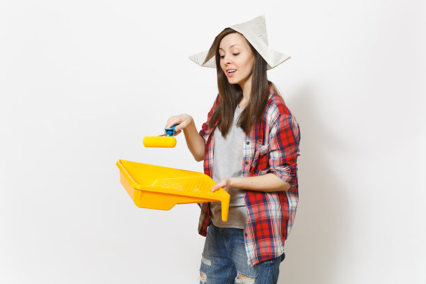 年轻关心美丽的女人在报纸帽子浸滚轮墙壁油漆托盘隔离在白色的背景。仪器，装修公寓的工具。修理家里的概念。图片下载