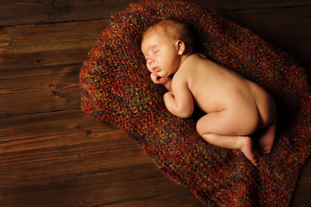 新生婴儿睡在棕色的毛毯上，新生的孩子在木头背景图片下载