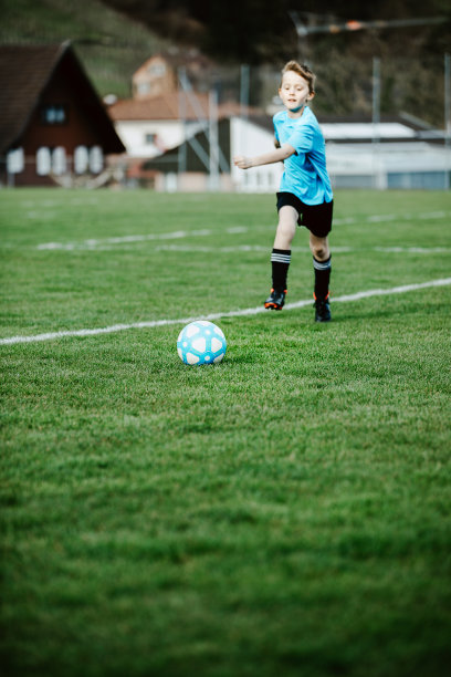 男孩在当地的体育场外面的草地上踢足球，跑着去踢球。下一球，注意球。孩子们踢足球，最爱的运动，全世界的足球热。图片下载