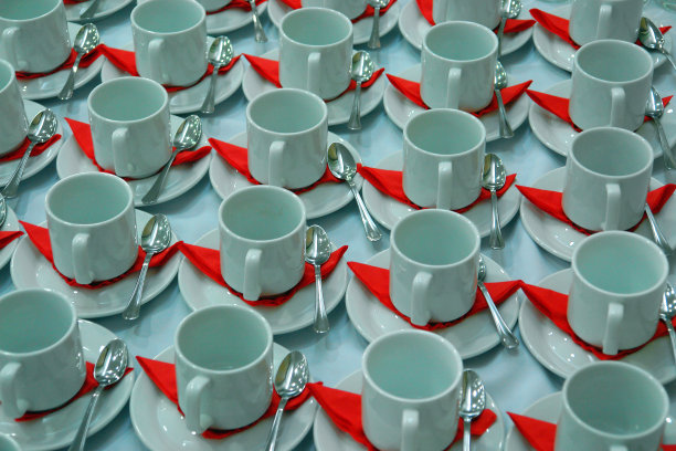 有许多排咖啡杯和咖啡碟，配有茶匙和一个红色盘子。白色和红色背景图片下载