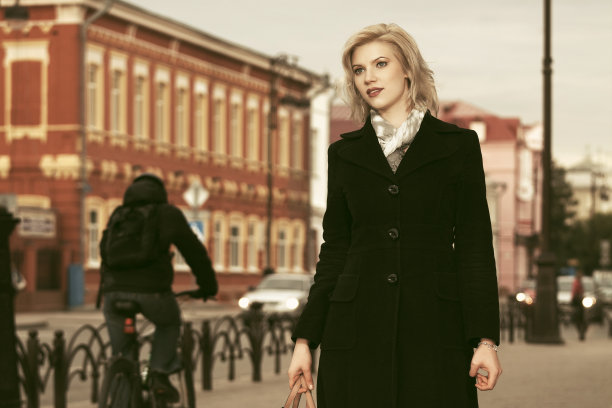 时尚的金发女人穿着黑色外套走在城市的街道上图片下载