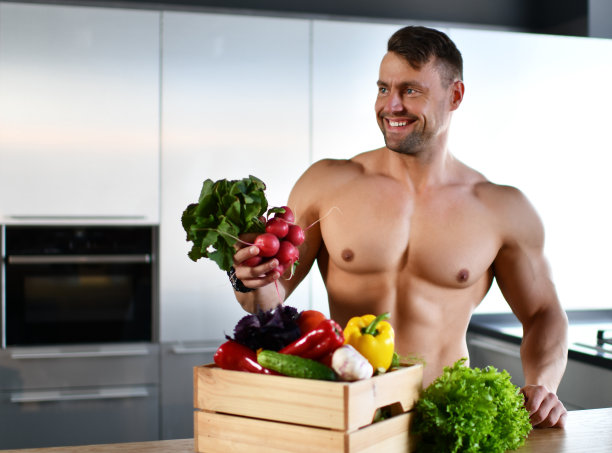 肌肉发达的运动员站在厨房蔬菜杂货手里拿着萝卜看着角落微笑图片下载