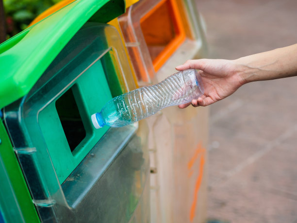 特写女子手扔空塑料水瓶在回收箱。素材图片