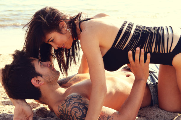 一对迷人的年轻夫妇躺在沙滩上。图片下载