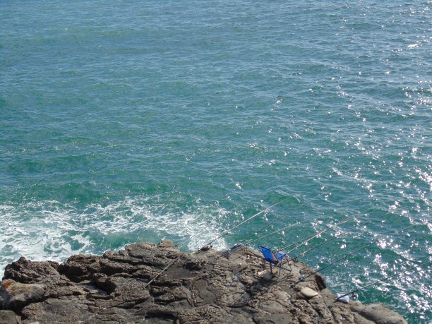 鱼竿和渔民空椅子在岩石的形成。图片下载