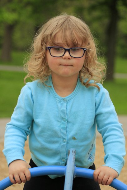 3到5岁的小女孩，戴着眼镜，穿着蓝色衬衫在学校操场上玩耍图片下载