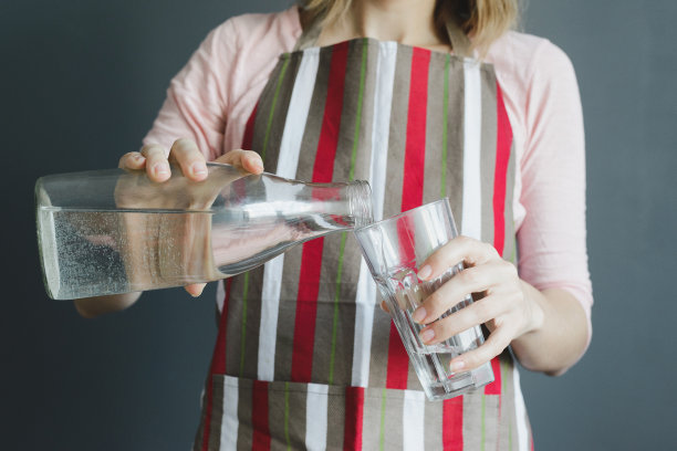 女人把水倒进灰色背景的玻璃杯里图片下载