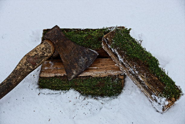 旧斧躺在长满青苔的圆木上，躺在雪中图片下载
