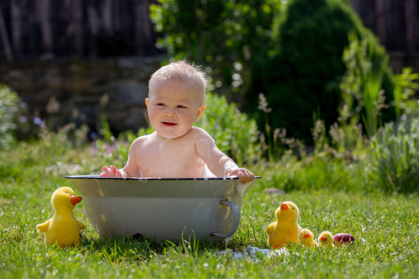 可爱的小男孩在水池里，在花园里用泡泡和鸭子玩具洗澡图片下载