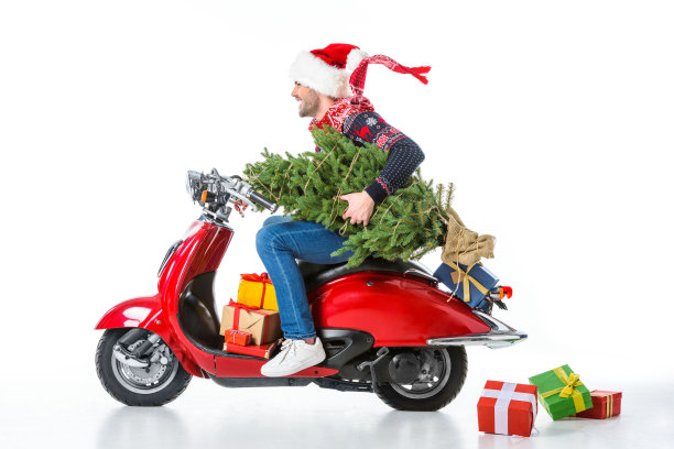 面带微笑的男人戴着圣诞帽和围巾捧着圣诞树，同时骑着红色的摩托车，散落的礼物躺在白色的地上，孤立无间图片下载