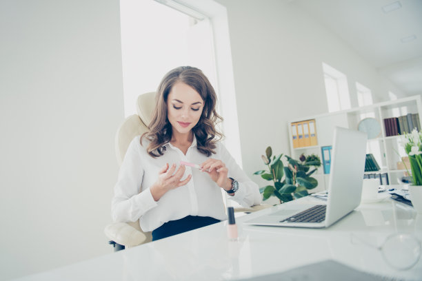 肖像漂亮，迷人，时尚，时髦，开朗的秘书与卷发做指甲在休息时间坐在桌面在现代办公室使用指甲锉图片下载