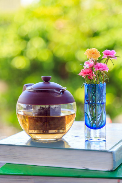 以自然为背景的书，茶壶和花瓶上的花。图片下载