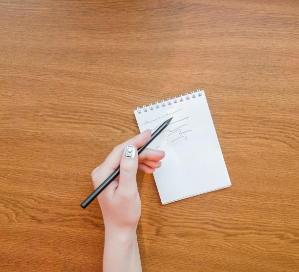 白色笔记本手写体女孩在木桌纹理的背景上写字。工作用的笔记本电脑和手机。概念艺术、设计、成功、创意、创业、工作、教育图片下载