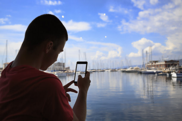年轻的游客，用触摸屏，用智能手机拍照，照片短信。欣赏航海船、码头的景色。意大利的里雅斯特，亚得里亚海。图片下载